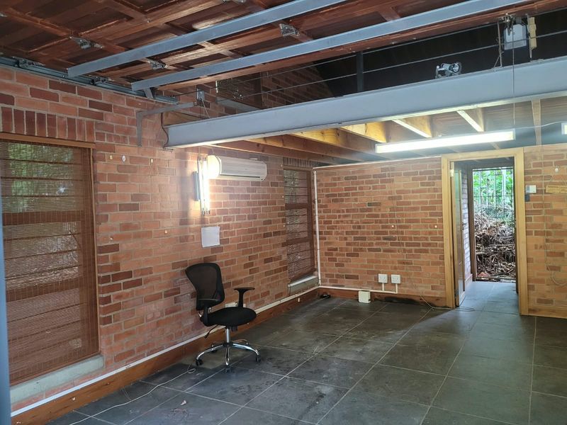 An open-plan office space featuring exposed brick walls, timber ceiling beams, and tiled flooring, offering a rustic industrial aesthetic suitable for a creative workspace.