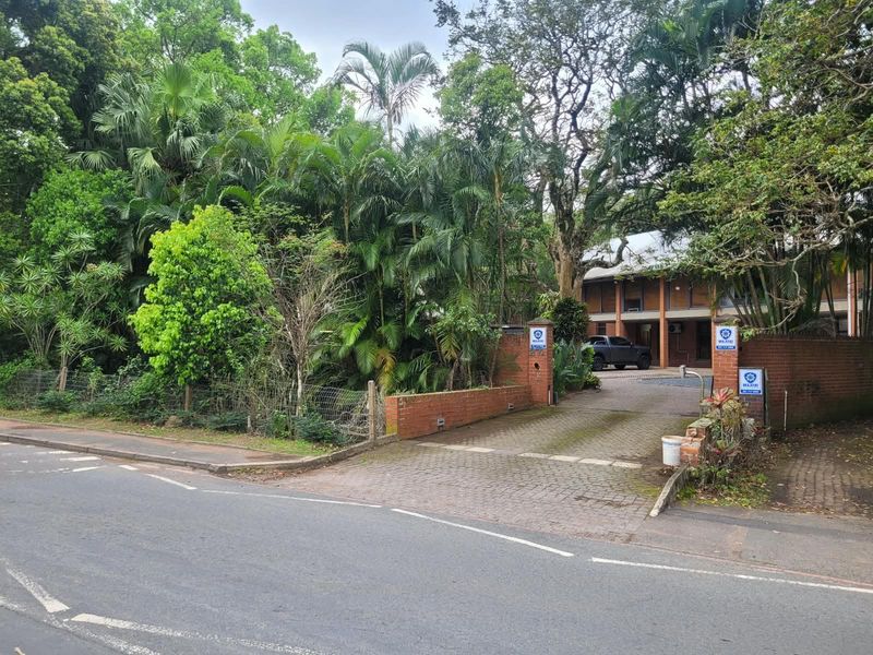 Front view of the office property featuring a paved driveway, brick boundary wall, and established garden surroundings.