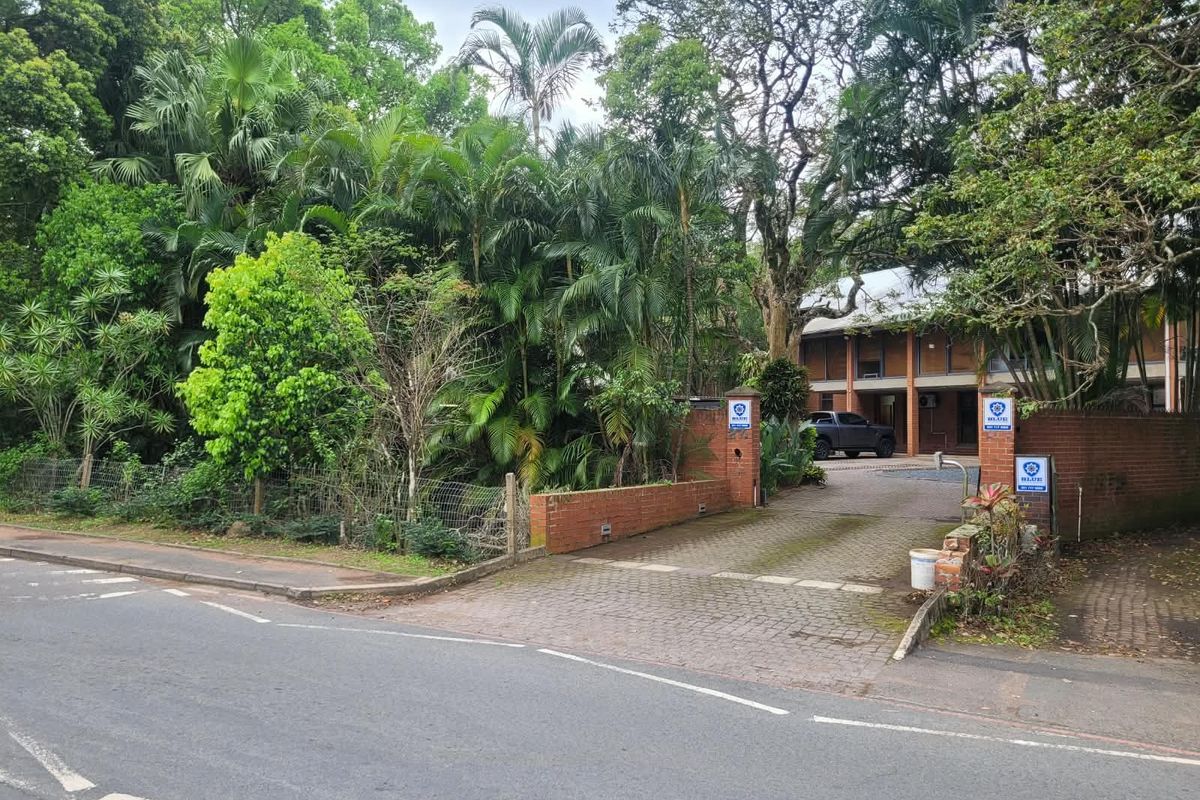 Front view of the office property featuring a paved driveway, brick boundary wall, and established garden surroundings.