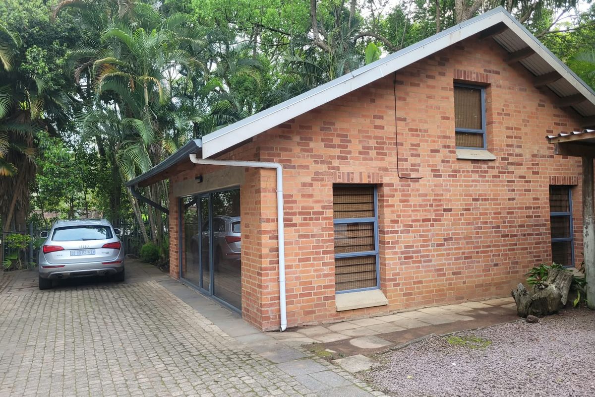 A well-maintained brick office building featuring modern aluminium window frames, a pitched roof, and a paved driveway set within a lush, green garden environment.