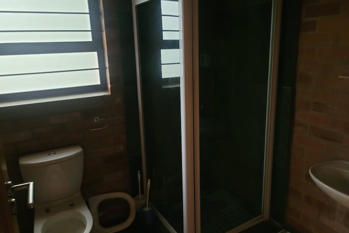 A compact bathroom featuring exposed brick walls, a shower enclosure, a toilet, and a wall-mounted basin with a louvre window.