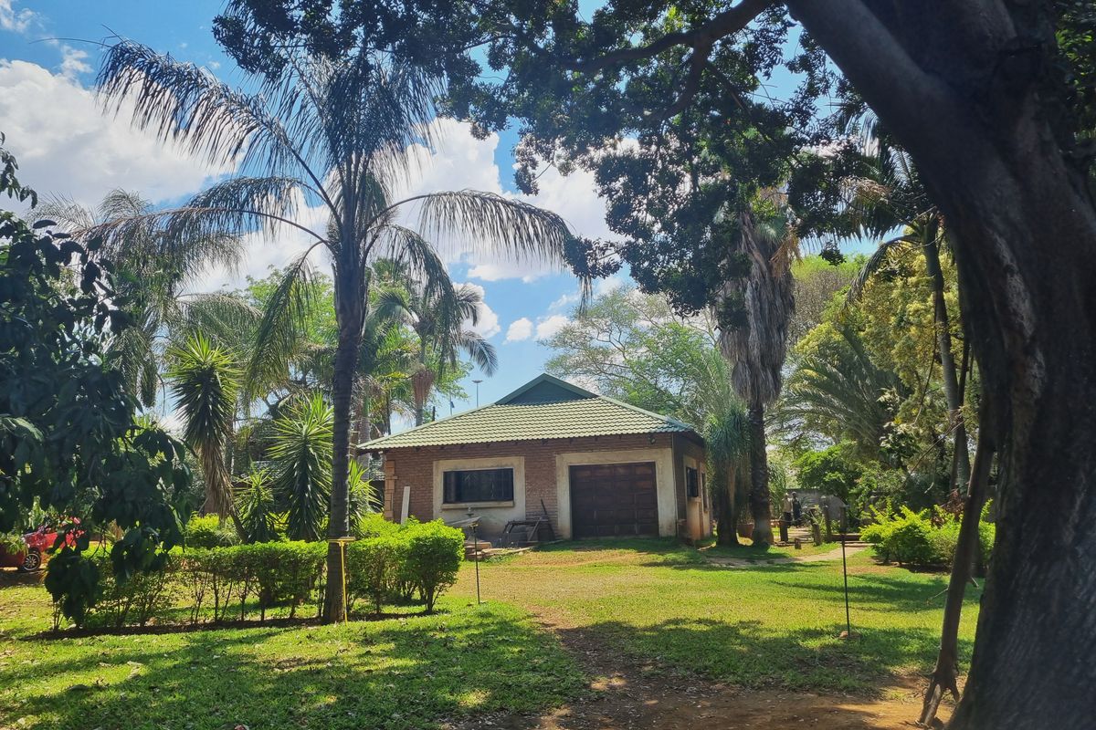 A view of a brick-built outbuilding or garage set within a mature, landscaped garden on a farm property.