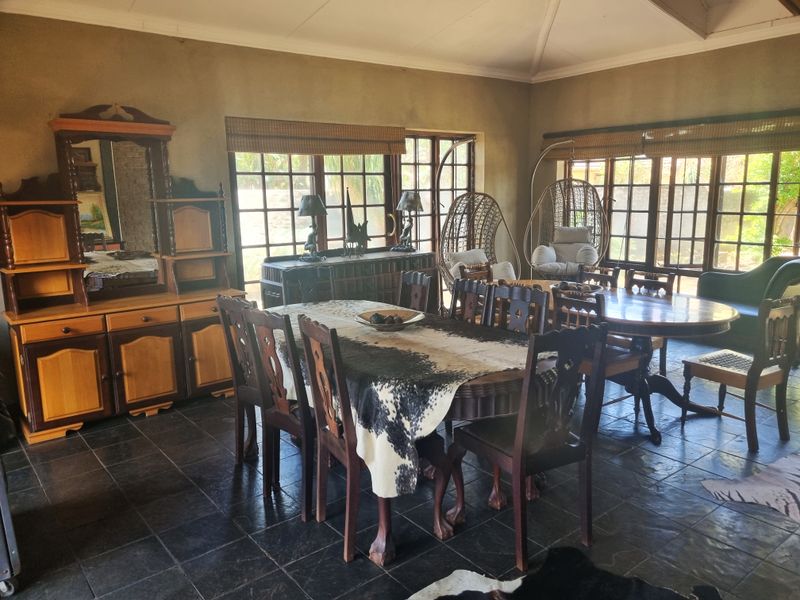 Spacious dining room featuring dark tiled flooring, vaulted ceilings, and large windows that provide ample natural light, creating a warm and inviting atmosphere.