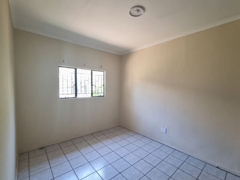 An empty bedroom featuring tiled flooring, a window with security bars, and a central ceiling light fixture.