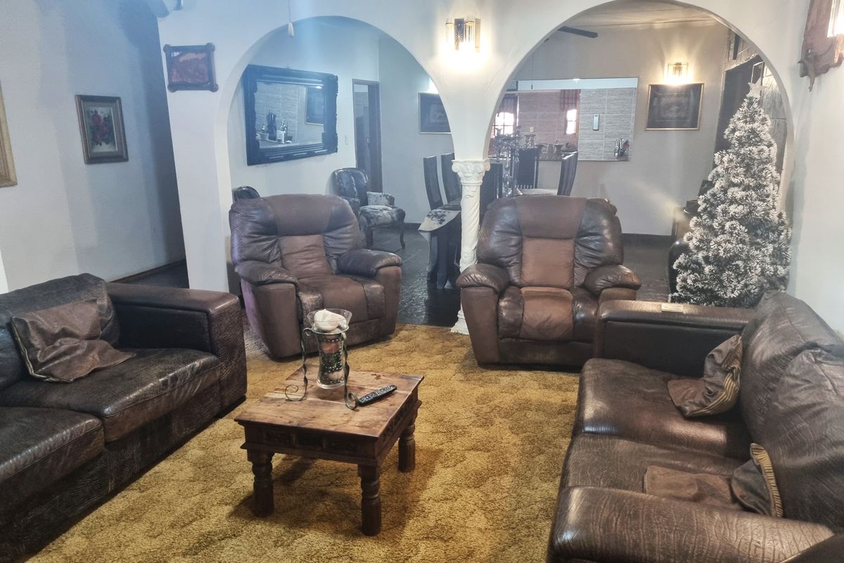 A spacious living room featuring classic arched doorways, decorative columns, and wall sconces, connecting to an adjacent dining area.