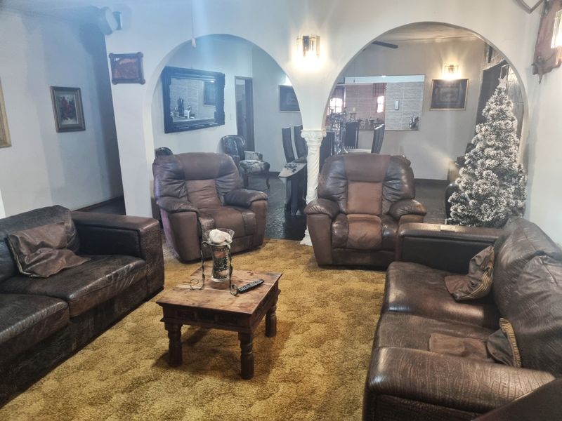 A spacious living room featuring classic arched doorways, decorative columns, and wall sconces, connecting to an adjacent dining area.
