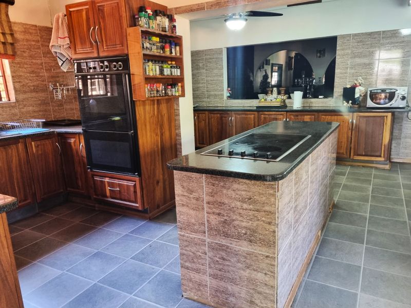 Spacious kitchen featuring extensive wooden cabinetry, a central island with a built-in electric cooktop, granite countertops, and tiled finishes throughout.