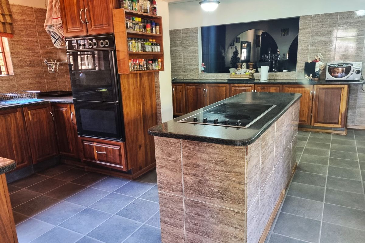 Spacious kitchen featuring extensive wooden cabinetry, a central island with a built-in electric cooktop, granite countertops, and tiled finishes throughout.