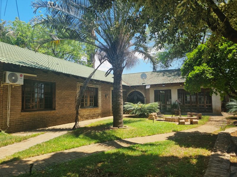 A view of the rear exterior of the farm property, featuring brick walls, a tiled roof, paved pathways, and established garden landscaping.