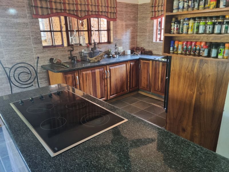 A functional kitchen featuring wooden cabinetry, granite countertops, and a built-in electric hob, with tiled walls and flooring throughout.