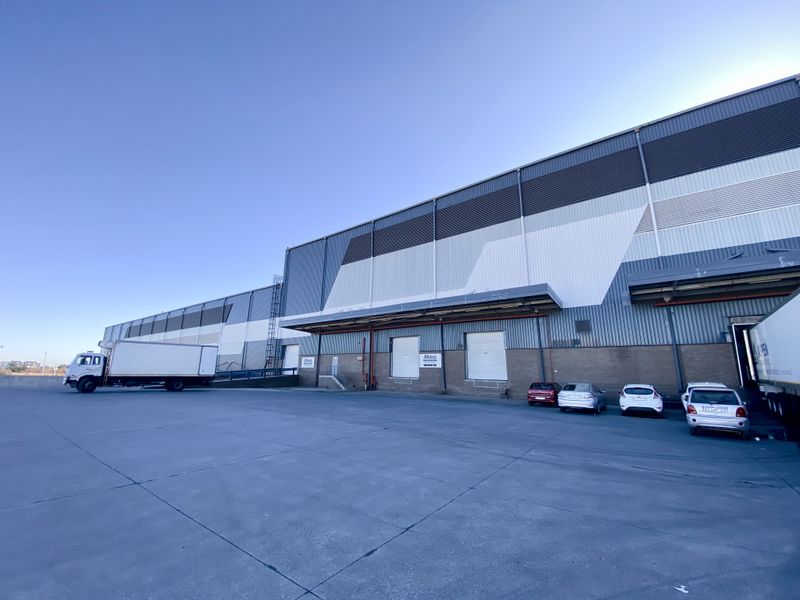 A wide-angle view of an industrial warehouse facility featuring multiple roller shutter loading doors, a spacious concrete yard, and modern metal cladding.