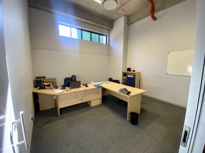 A functional office space featuring an exposed concrete ceiling, fire sprinkler system, and high-level clerestory window for natural light.