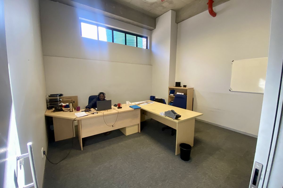 A functional office space featuring an exposed concrete ceiling, fire sprinkler system, and high-level clerestory window for natural light.