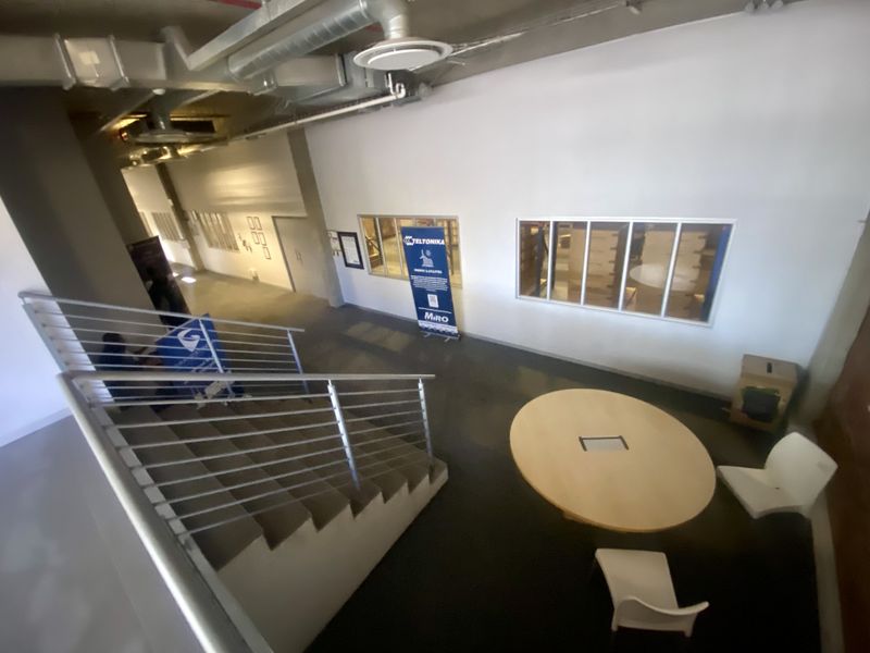 Industrial style hallway featuring exposed ceiling ductwork, a concrete staircase with metal balustrades, and internal windows overlooking adjacent office spaces.
