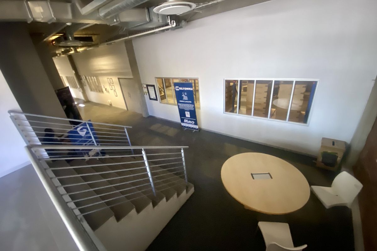 Industrial style hallway featuring exposed ceiling ductwork, a concrete staircase with metal balustrades, and internal windows overlooking adjacent office spaces.