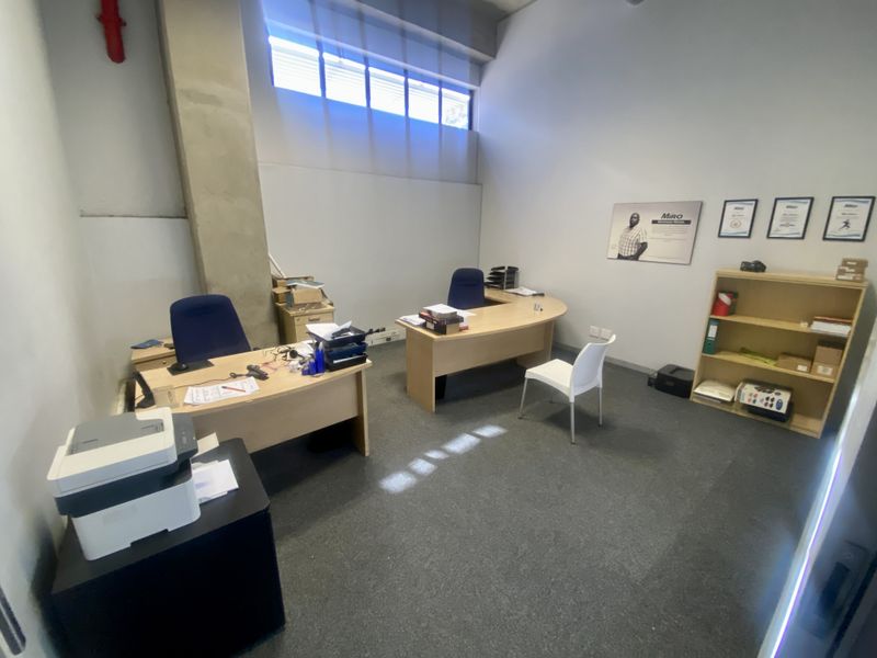 Functional office space featuring high-level clerestory windows, exposed concrete structural elements, and carpeted flooring, suitable for a professional industrial or commercial workspace.