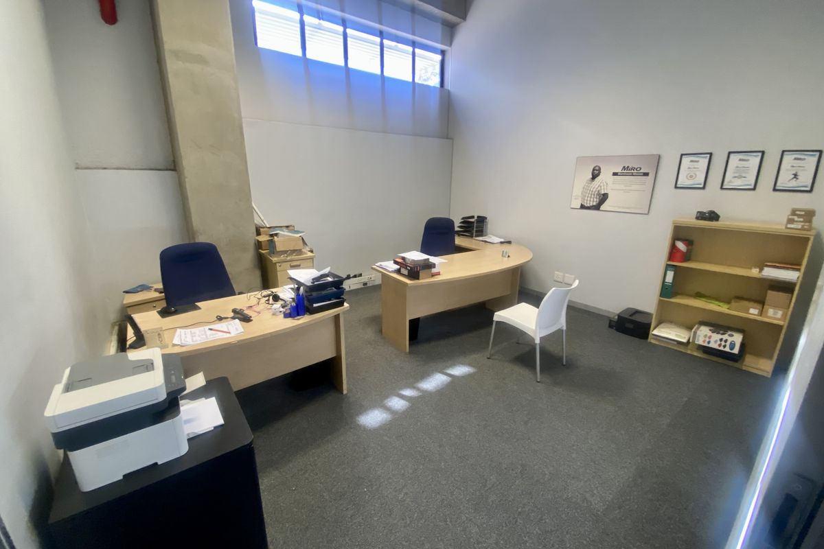 Functional office space featuring high-level clerestory windows, exposed concrete structural elements, and carpeted flooring, suitable for a professional industrial or commercial workspace.