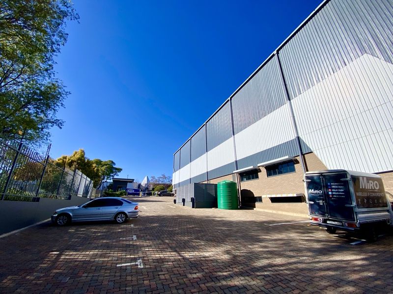 Industrial property exterior featuring a large metal-clad warehouse, brick facade, paved parking area, and secure perimeter fencing.