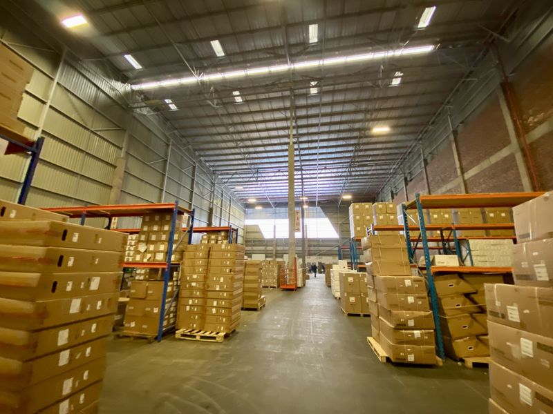 Spacious industrial warehouse featuring high-bay lighting, exposed steel roof structure, and extensive heavy-duty steel racking systems for efficient storage and logistics operations.