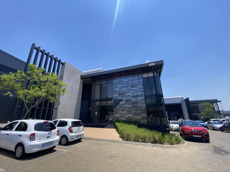 Modern industrial office building facade featuring contemporary metal cladding, extensive glass glazing, and a paved entrance area.
