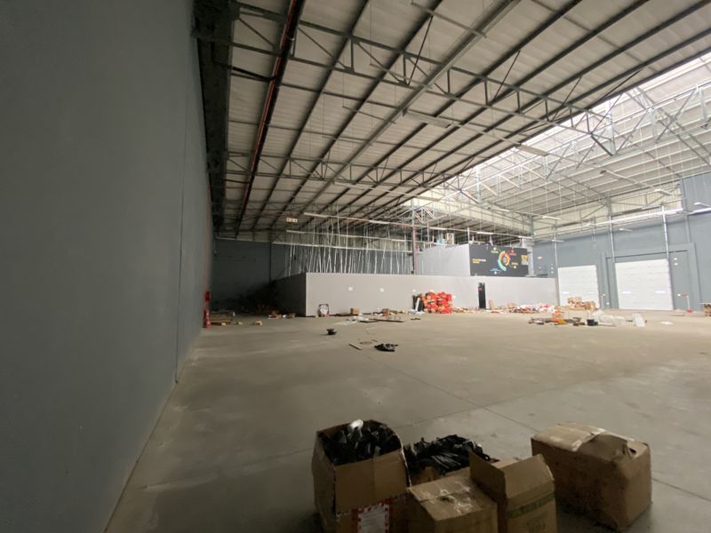 Spacious industrial warehouse unit featuring high ceilings with exposed steel trusses, concrete flooring, and large roller shutter doors for easy access.