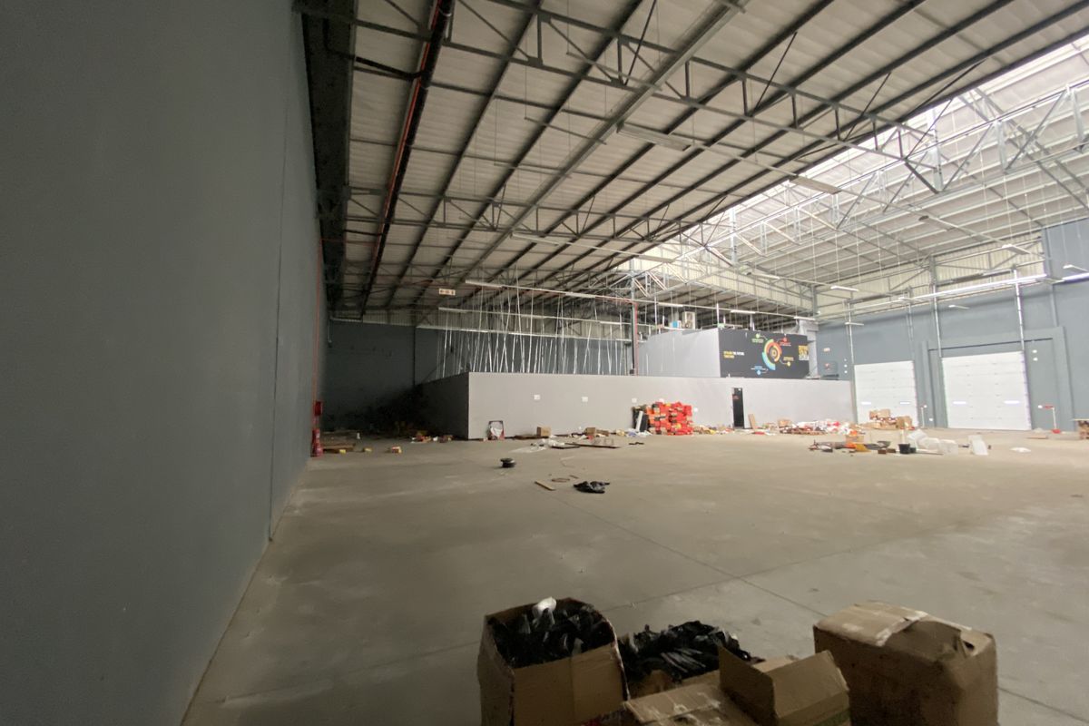 Spacious industrial warehouse unit featuring high ceilings with exposed steel trusses, concrete flooring, and large roller shutter doors for easy access.