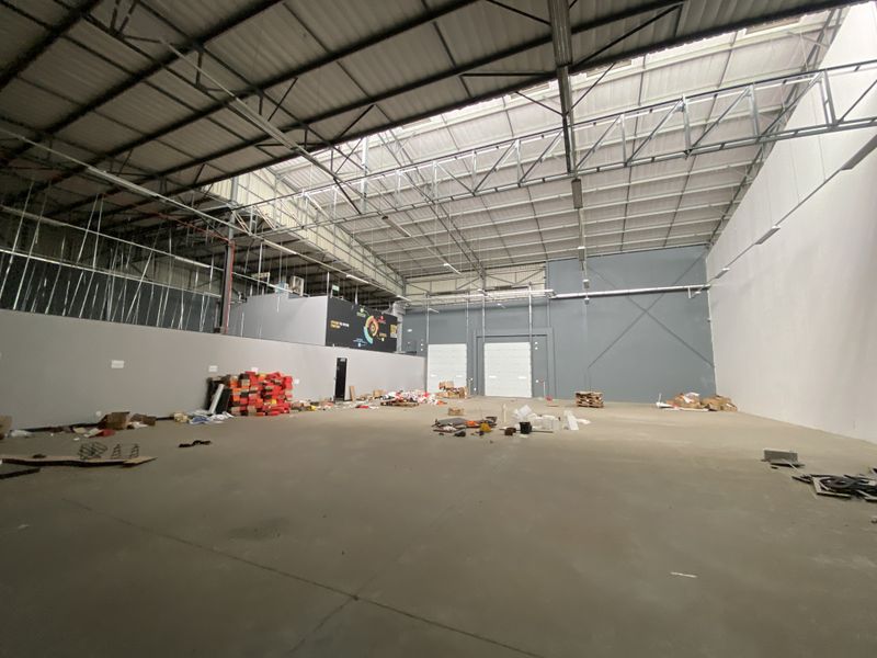 Spacious industrial warehouse unit featuring high ceilings with exposed steel trusses, concrete flooring, and large roller shutter doors for easy access.
