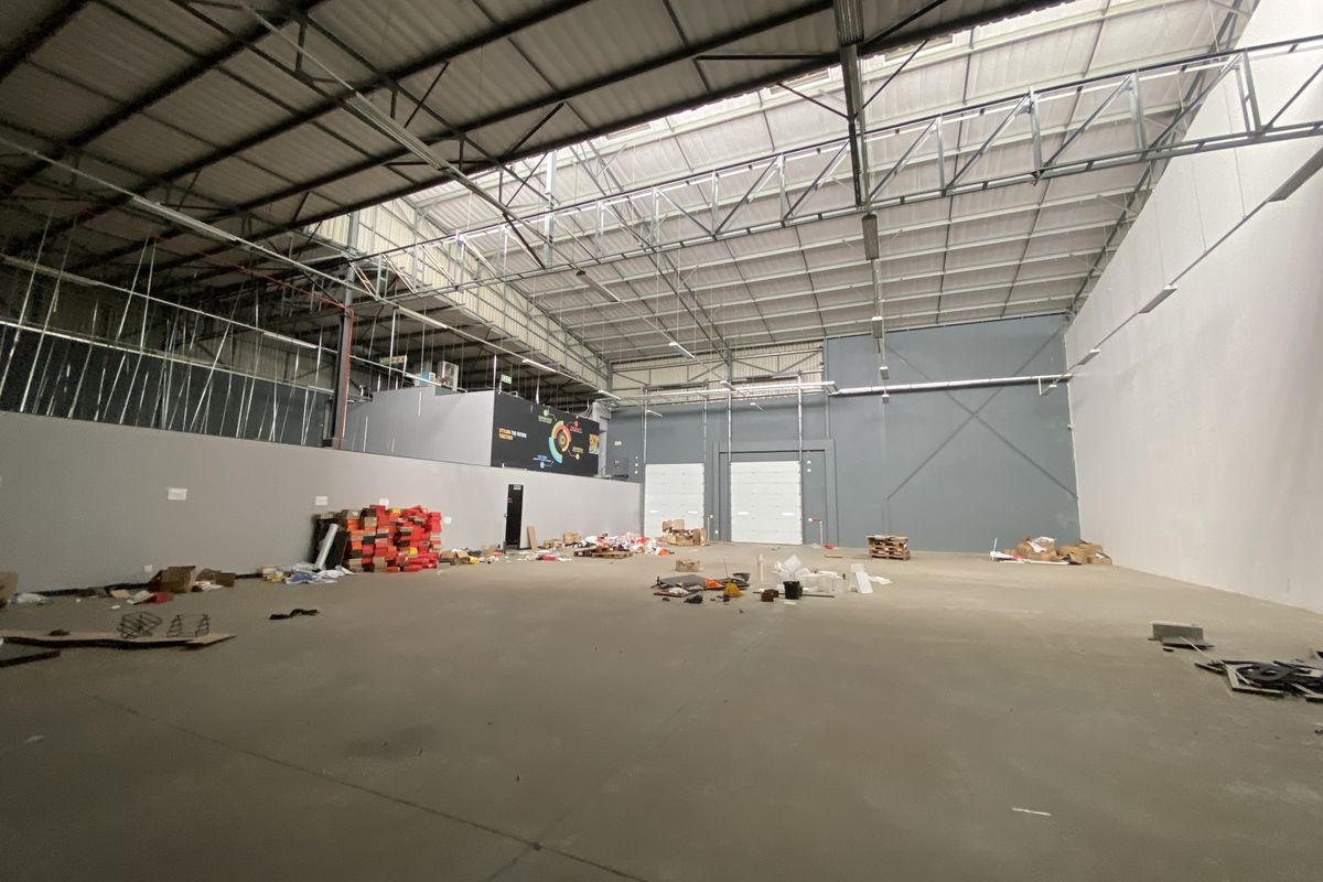 Spacious industrial warehouse unit featuring high ceilings with exposed steel trusses, concrete flooring, and large roller shutter doors for easy access.