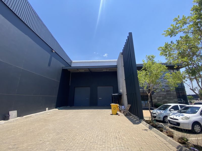 Rear industrial loading area featuring dual roller shutter doors, paved yard space, and modern metal cladding with architectural design elements.
