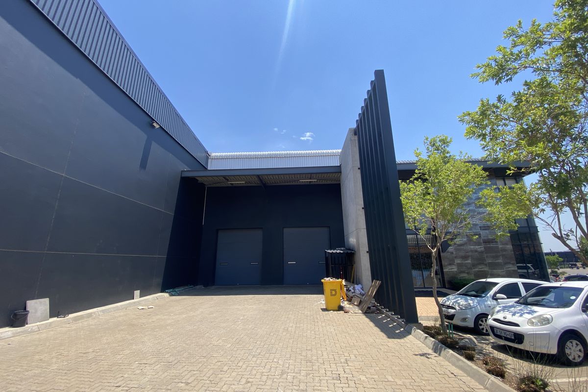 Rear industrial loading area featuring dual roller shutter doors, paved yard space, and modern metal cladding with architectural design elements.