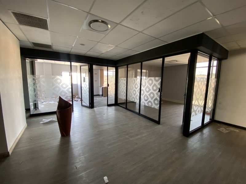 Open plan office space featuring modern glass partitions, suspended ceilings with recessed lighting, and durable vinyl flooring.