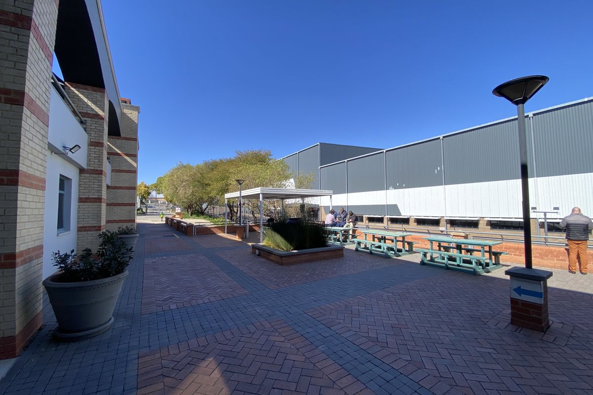 A well-maintained paved outdoor courtyard area featuring brick and metal industrial building facades, raised planter beds, and integrated exterior lighting.