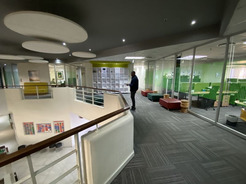 Spacious office hallway featuring glass-partitioned workspaces, modern acoustic ceiling panels, recessed lighting, and a built-in shelving unit.