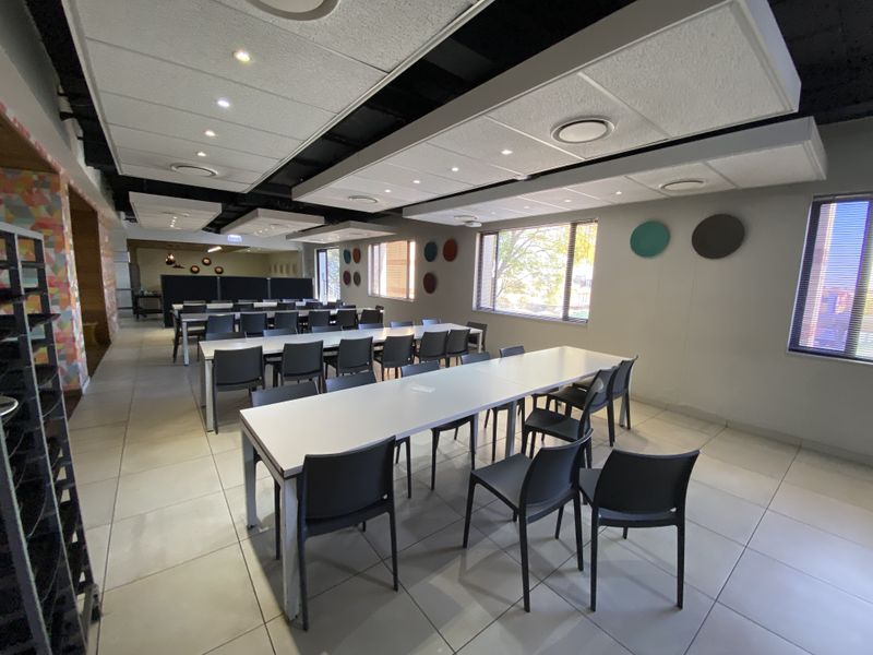 Spacious industrial office area featuring tiled flooring, suspended ceilings with recessed lighting, and large windows providing ample natural light.