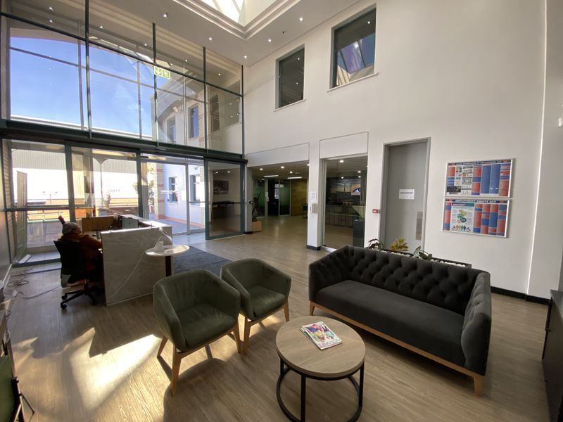 Bright and modern industrial reception area featuring double-volume ceilings, a large skylight, floor-to-ceiling glass windows, and professional laminate flooring.
