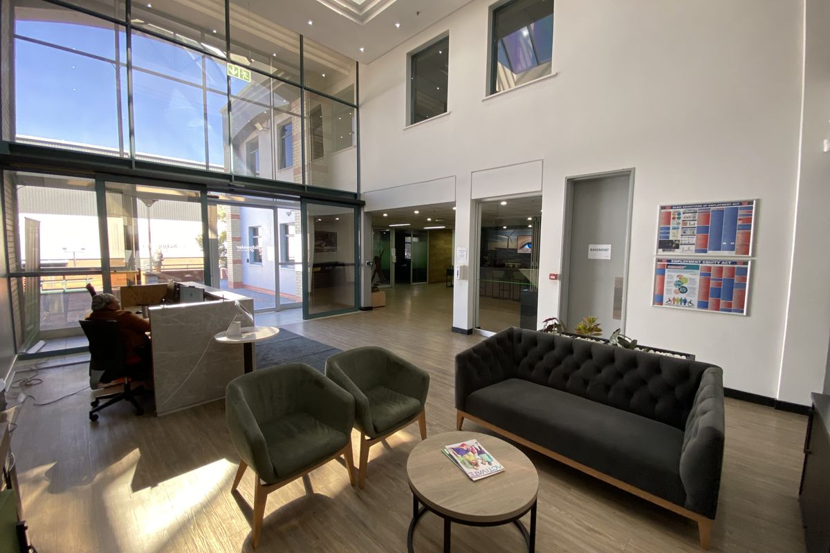 Bright and modern industrial reception area featuring double-volume ceilings, a large skylight, floor-to-ceiling glass windows, and professional laminate flooring.