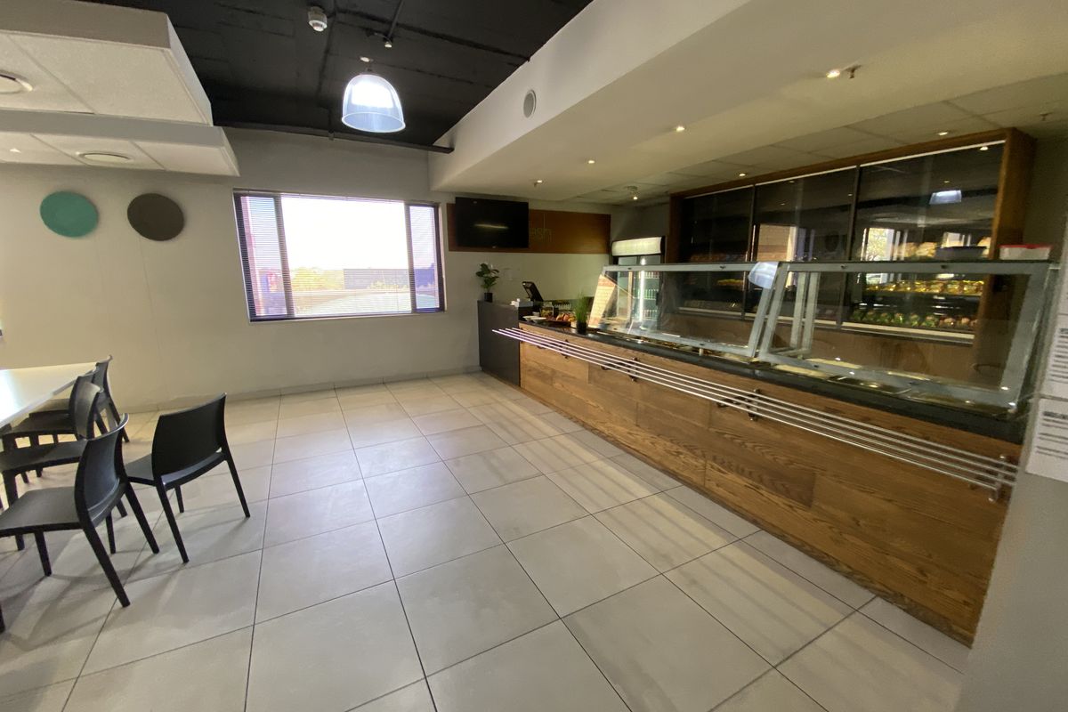 Commercial kitchen or cafe service area featuring a wooden service counter, glass display units, and tiled flooring in an industrial setting.