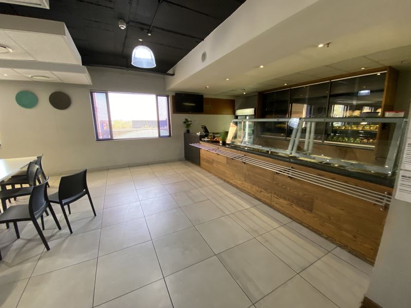 Commercial kitchen or cafe service area featuring a wooden service counter, glass display units, and tiled flooring in an industrial setting.