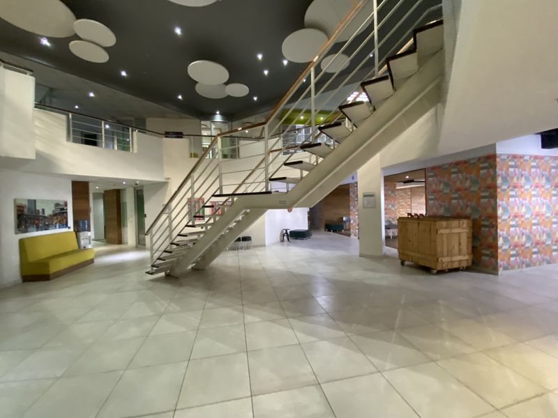 Spacious industrial-style entrance lobby featuring a prominent central staircase, tiled flooring, and modern acoustic ceiling detailing.