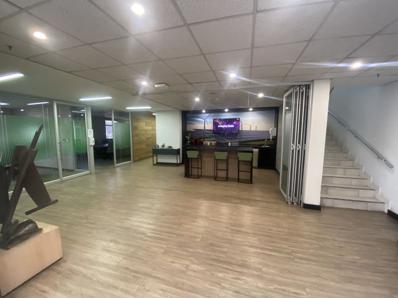 Spacious open-plan industrial office area featuring a built-in kitchenette, glass partitions, modern laminate flooring, and a staircase leading to the upper level.
