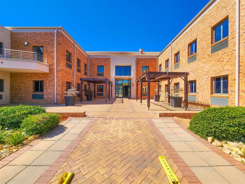 A well-maintained office building courtyard featuring brick facades, paved walkways, and timber pergolas, providing a professional and inviting outdoor space.