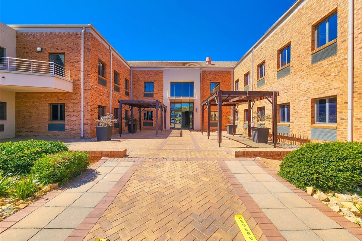 A well-maintained office building courtyard featuring brick facades, paved walkways, and timber pergolas, providing a professional and inviting outdoor space.
