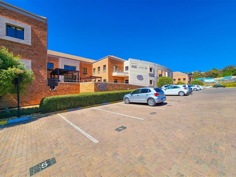 A professional exterior view of a modern face brick office building featuring a paved parking area and landscaped garden surrounds.
