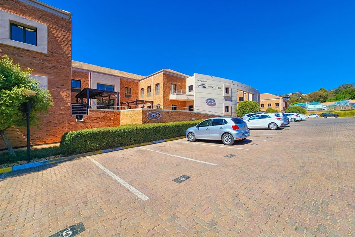 A professional exterior view of a modern face brick office building featuring a paved parking area and landscaped garden surrounds.