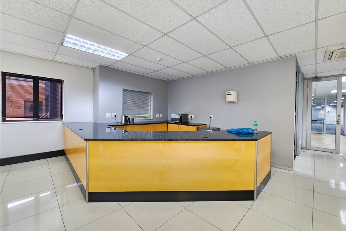 A clean, functional office kitchenette featuring light wood cabinetry, dark granite countertops, tiled flooring, and a drop ceiling with integrated lighting.