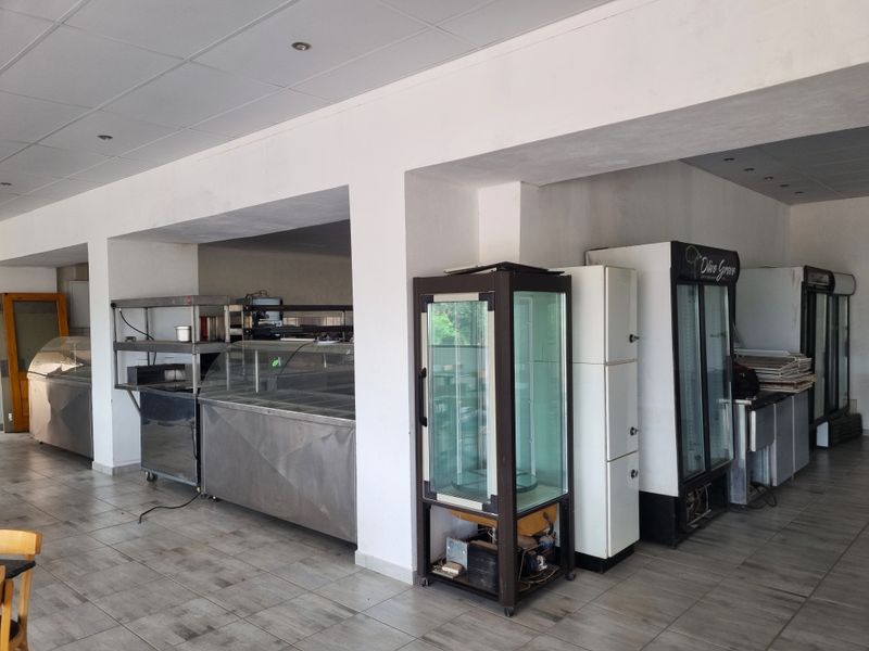 A commercial kitchen area featuring stainless steel prep counters, display refrigeration units, and tiled flooring, suitable for guest house catering operations.