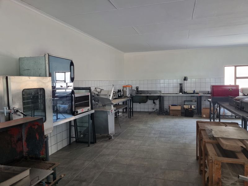 A functional commercial-style kitchen area featuring tiled flooring, wall-mounted splashbacks, and stainless steel prep surfaces, suitable for high-volume food preparation.