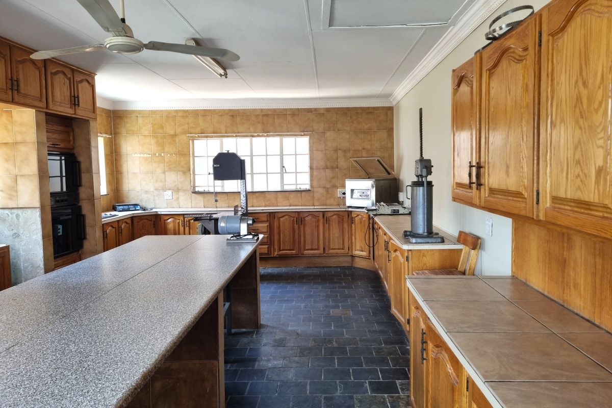 Spacious kitchen featuring extensive wooden cabinetry, stone-look countertops, tiled backsplash, and durable slate flooring, offering a functional layout for food preparation.