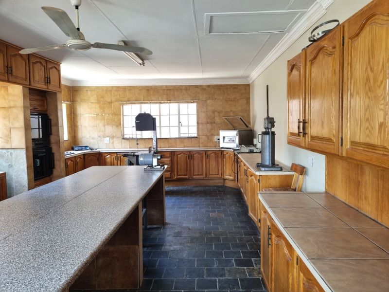 Spacious kitchen featuring extensive wooden cabinetry, stone-look countertops, tiled backsplash, and durable slate flooring, offering a functional layout for food preparation.