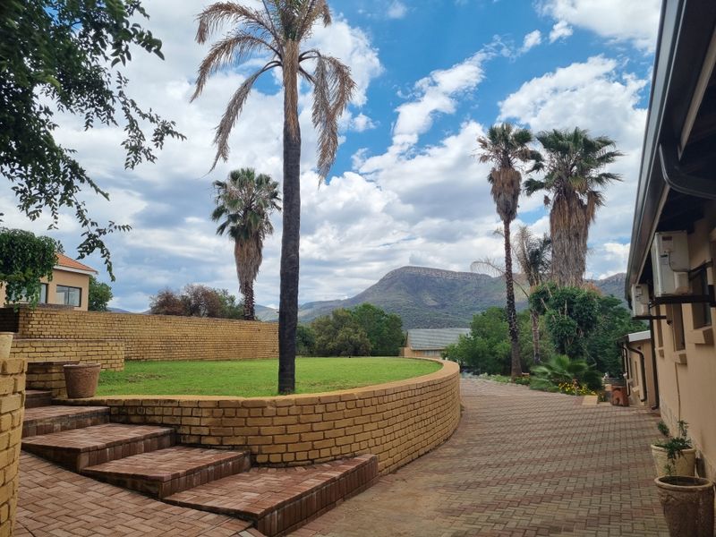 Rear exterior view featuring a brick paved driveway, tiered lawn with a curved brick retaining wall, and mountain views.